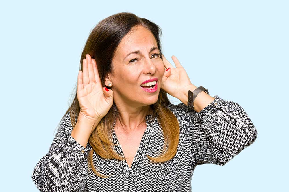 Smiling woman cupping both hands behind her ears to hear better, as when hearing aids sound uneven, from Port Elgin Audiology in Port Elgin, ON